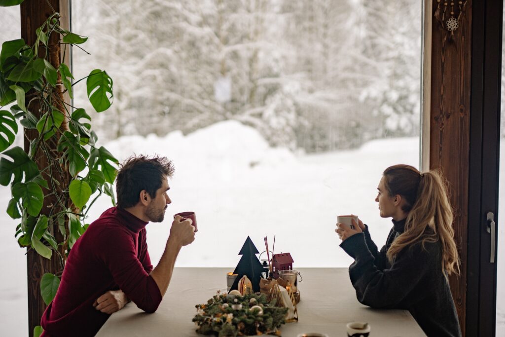 A couple sitting at a table next to a window with a view of snow outside.