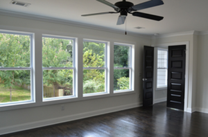 A row of 4 double-hung windows in a white room with dark floors and a ceiling fan.