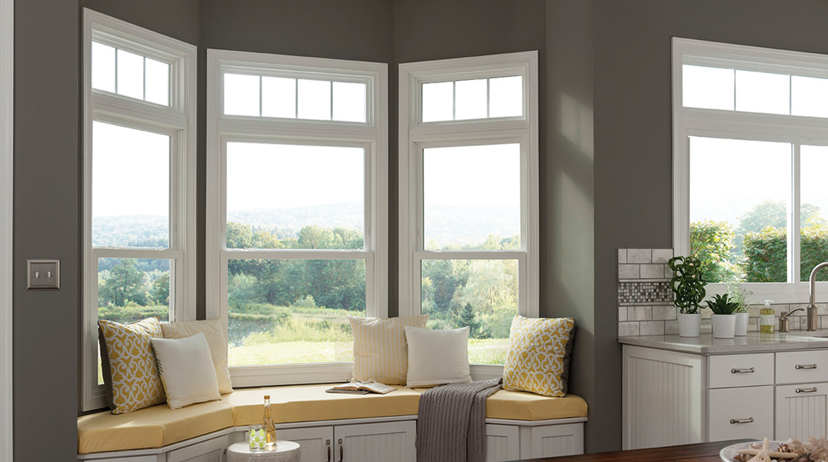 Vinyl bay windows over a yellow-cushioned reading a nook, overlooking wooded area from a hill.