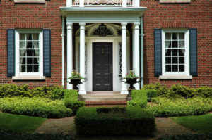 Black front door in large brick home with white columns on either side of the door.