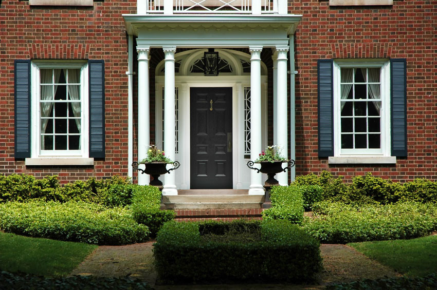 New black front door on large brick home with landscaping and white columns on either side of front step.