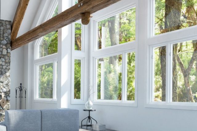 Double-pane white vinyl windows installed in an updated living room, looking out on greenery and trees.
