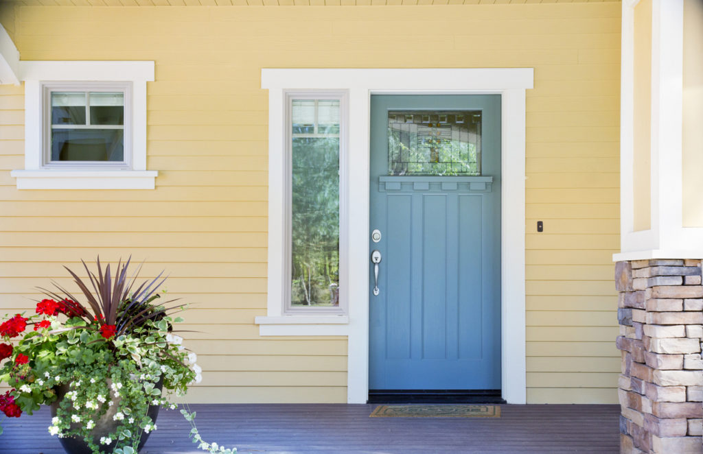 Baby blue Craftsman-style front door with textured glass and sidelite on pale yellow home.