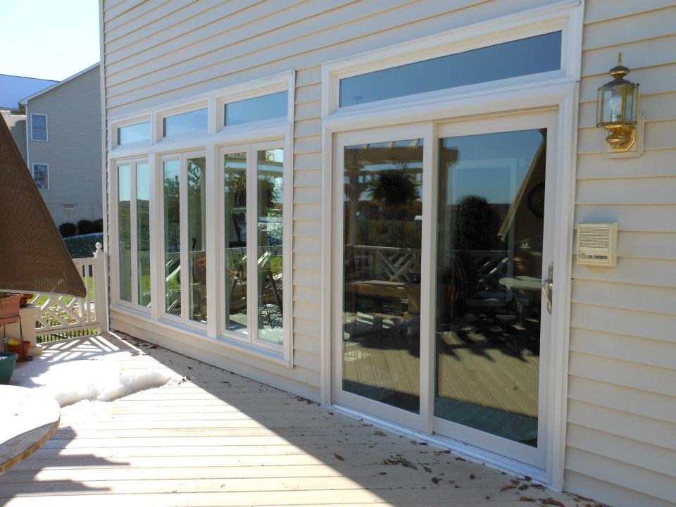 large windows and white sliding glass door on house with white siding. Exterior view from a deck.
