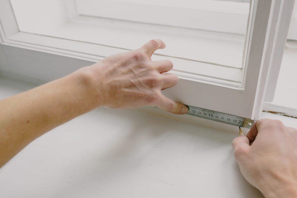 Close-up of hands measuring the length of a window with measuring tape.